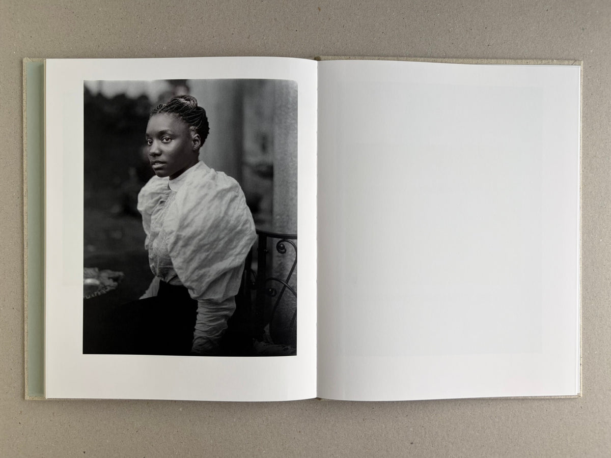 Black-and-white portrait of a woman on the left page of Dear God, the Parthenon is still broken, with a blank right page.