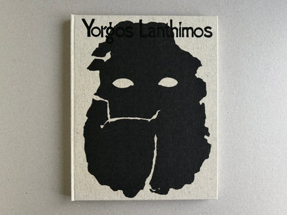 Front cover of Dear God, the Parthenon is still broken by Yorgos Lanthimos, showing the title on a cloth hardcover with a black abstract face-like graphic.