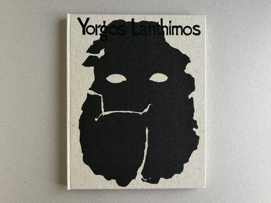 Front cover of Dear God, the Parthenon is still broken by Yorgos Lanthimos, showing the title on a cloth hardcover with a black abstract face-like graphic.