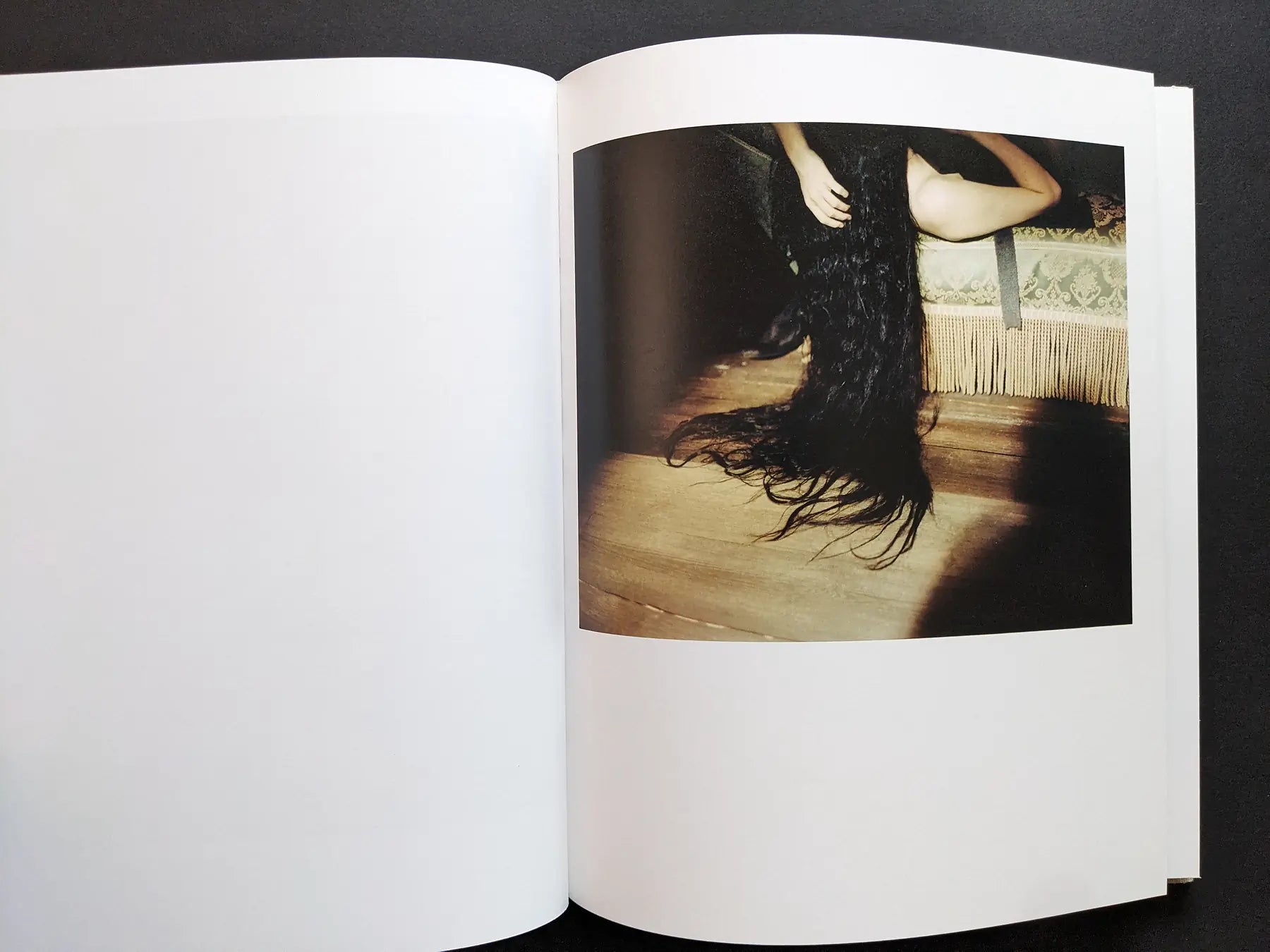 Color photograph of long dark hair draped over a bed in a staged interior.