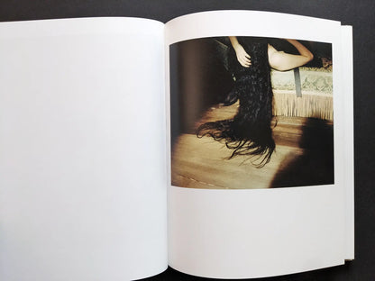 Color photograph of long dark hair draped over a bed in a staged interior.