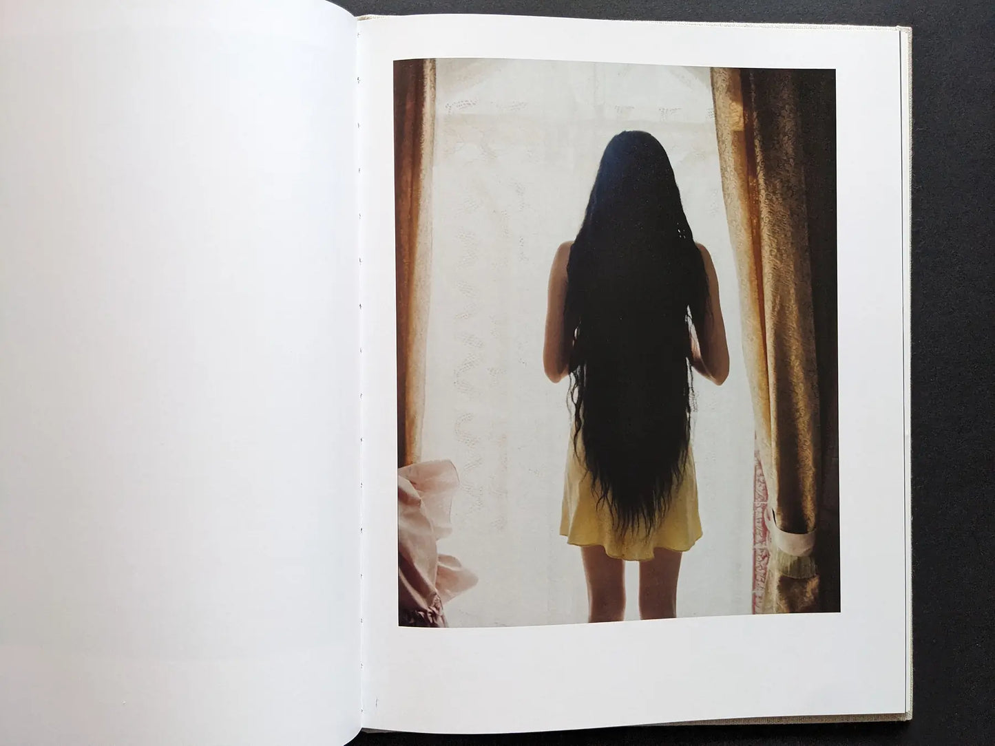 Color photograph of a woman with very long dark hair facing a window.