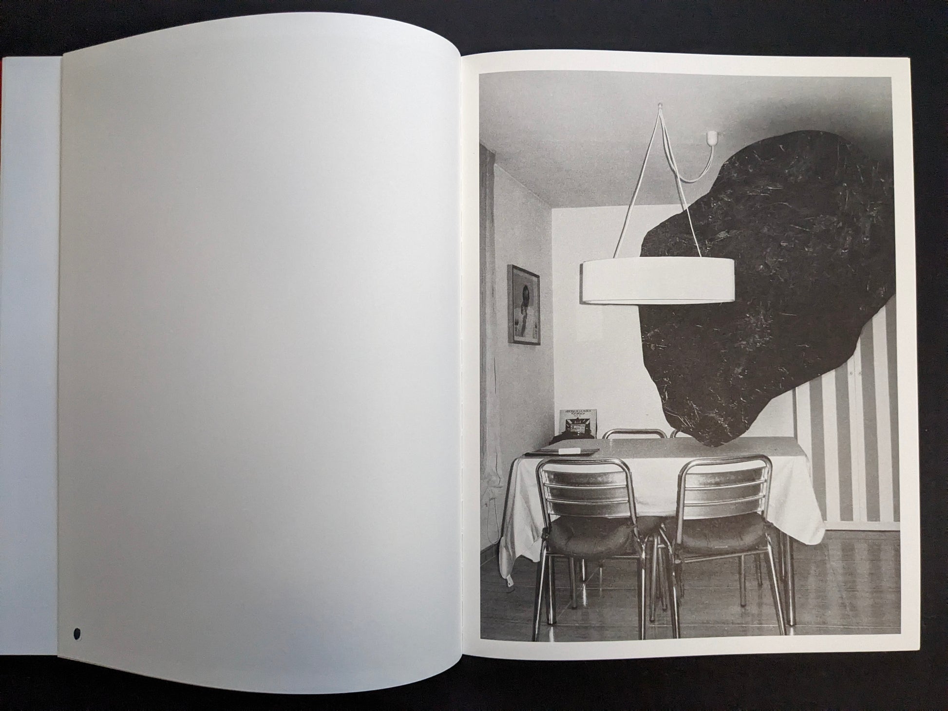 Interior page with a monochrome photograph of a dining table and chairs under a hanging lamp, with a dark wall shape behind.