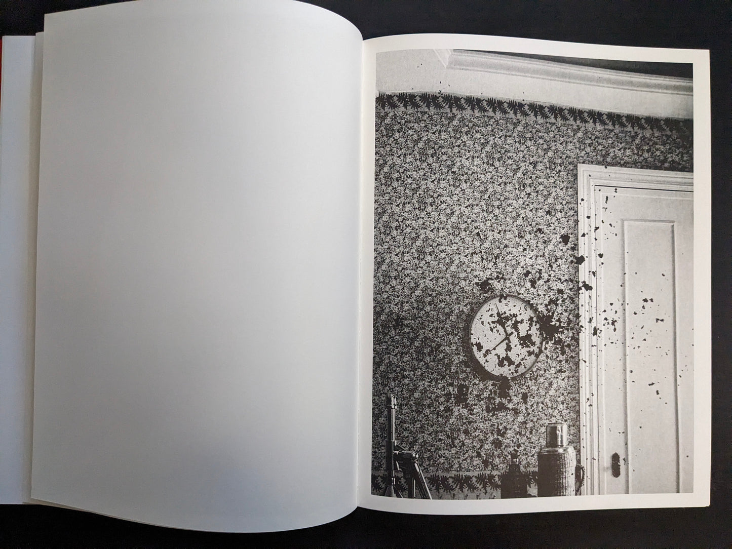 Interior page with a monochrome photograph of a patterned wall with a clock and a door marked with splatters.