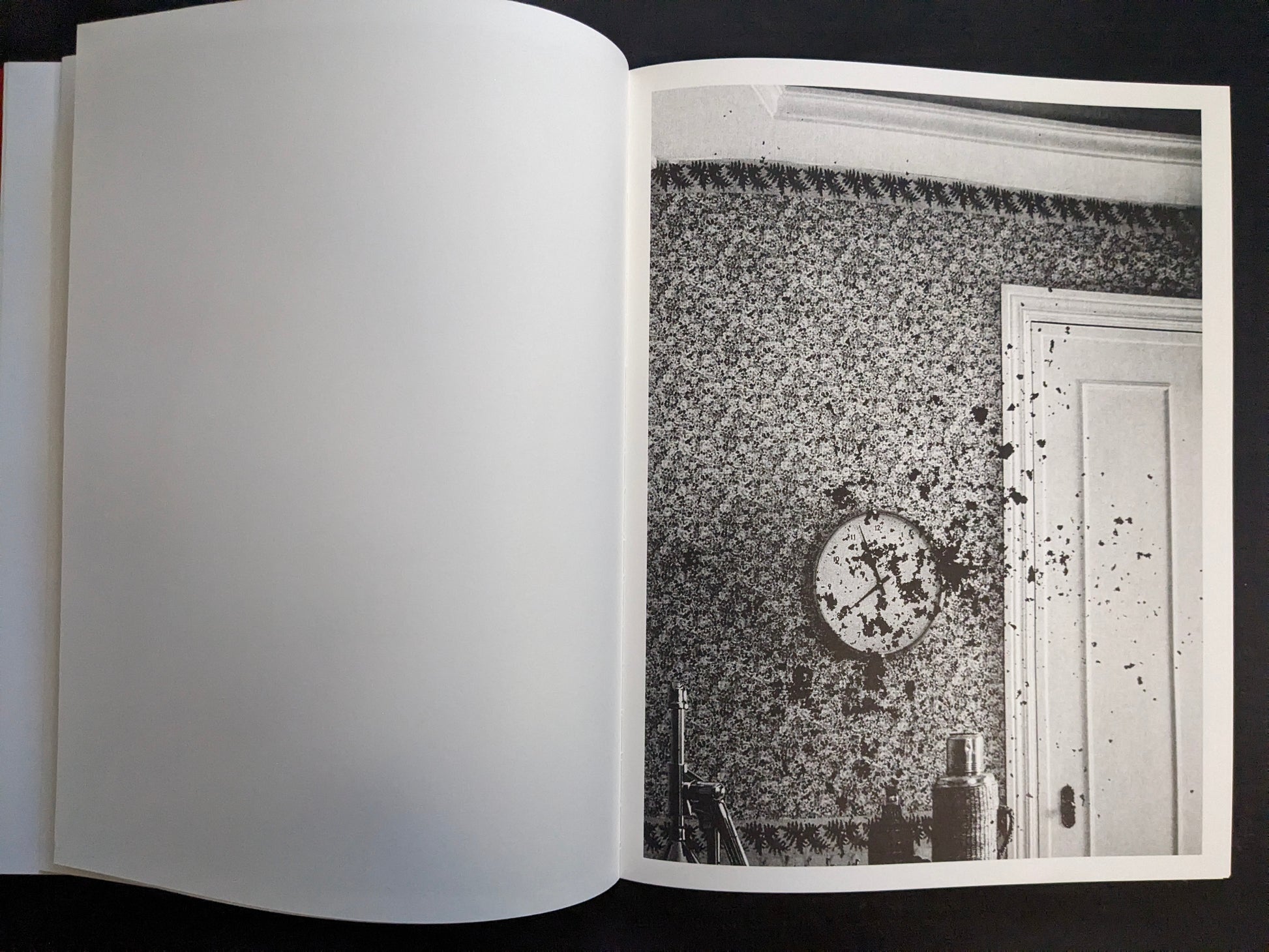 Interior page with a monochrome photograph of a patterned wall with a clock and a door marked with splatters.