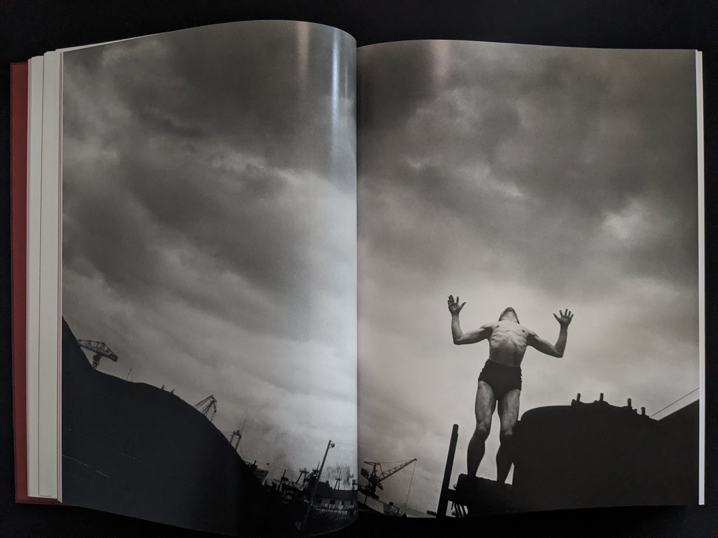 Black-and-white image of a man raising his arms against an industrial skyline