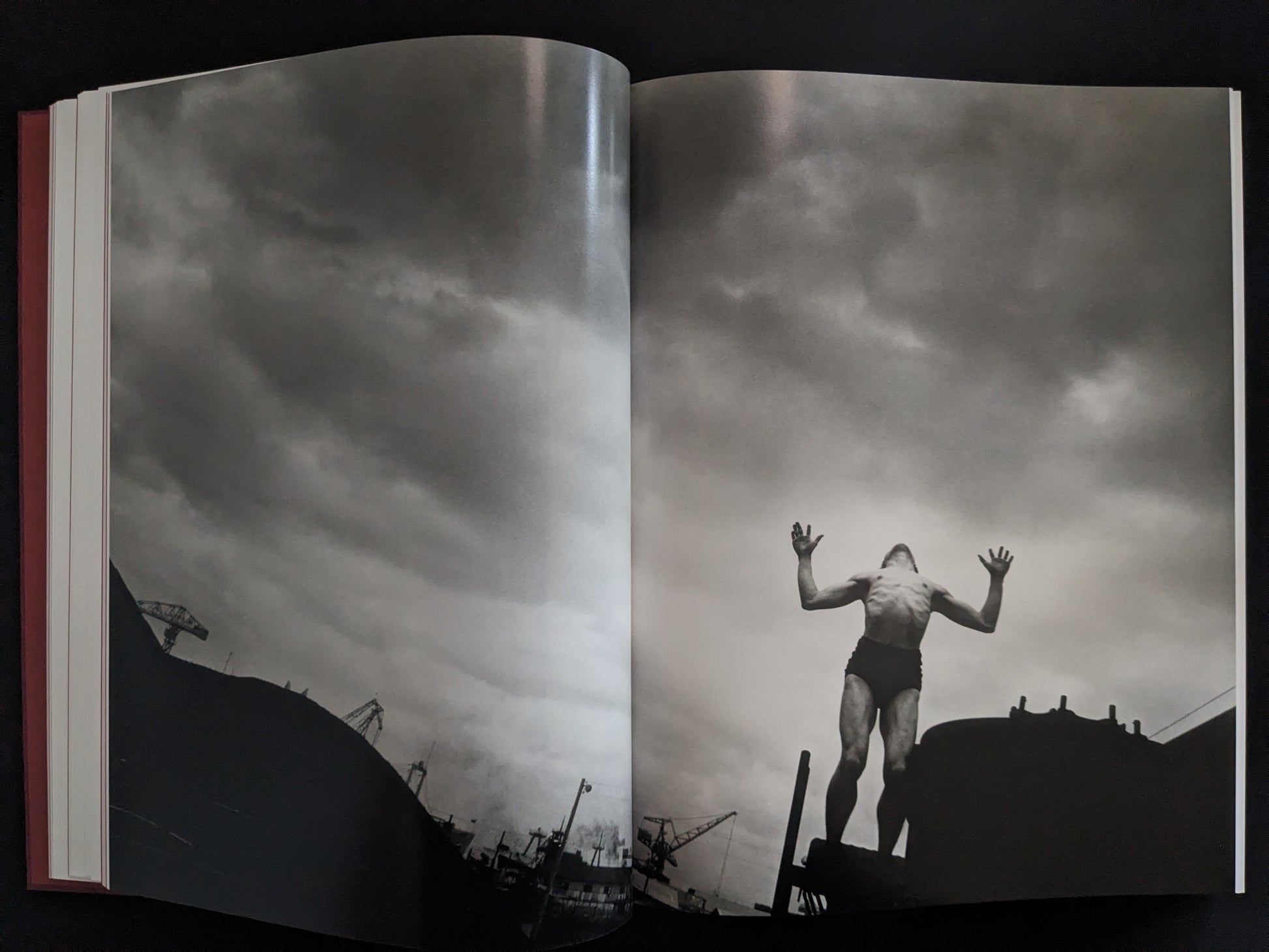 Black-and-white image of a man raising his arms against an industrial skyline