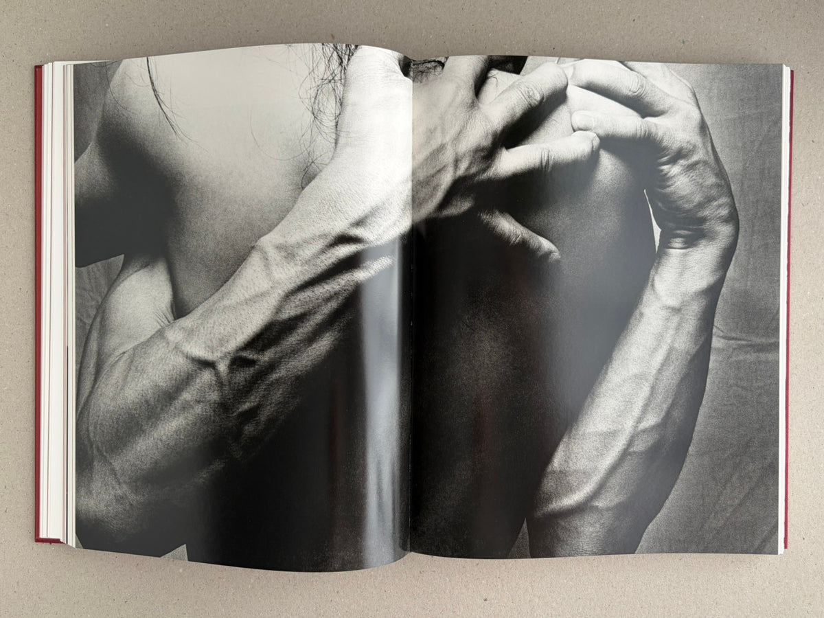 Open spread from Eikoh Hosoe, showing a black-and-white full-bleed photograph of a person’s torso and arms with hands framing the face.