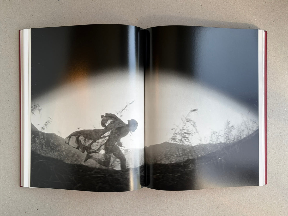 Open spread from Eikoh Hosoe, showing a black-and-white photograph of a running figure across a landscape.
