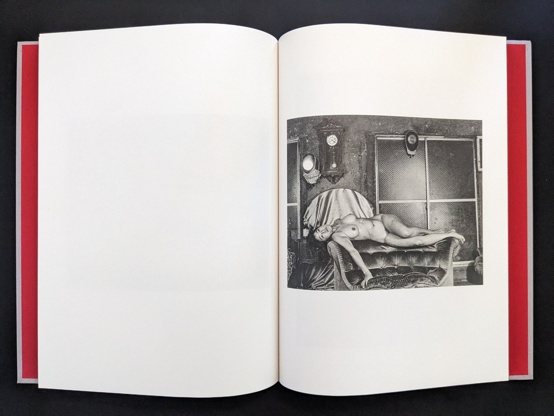 Black-and-white nude portrait of a woman reclining on a bed in a staged room from Eros Lost.