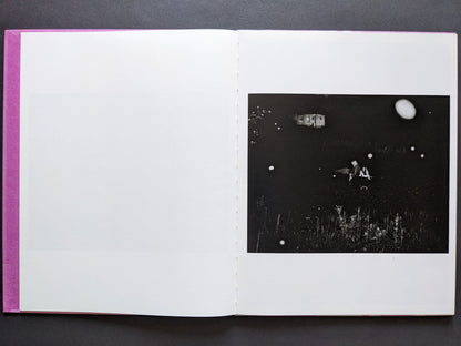 Night scene with two people in a boat, distant house, and floating white orbs in the dark, from "Flowers Drink the River."