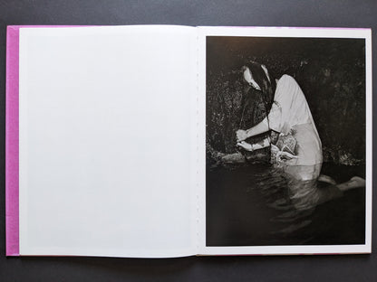 Portrait of a woman kneeling in water, washing her long hair in a cave-like setting.
