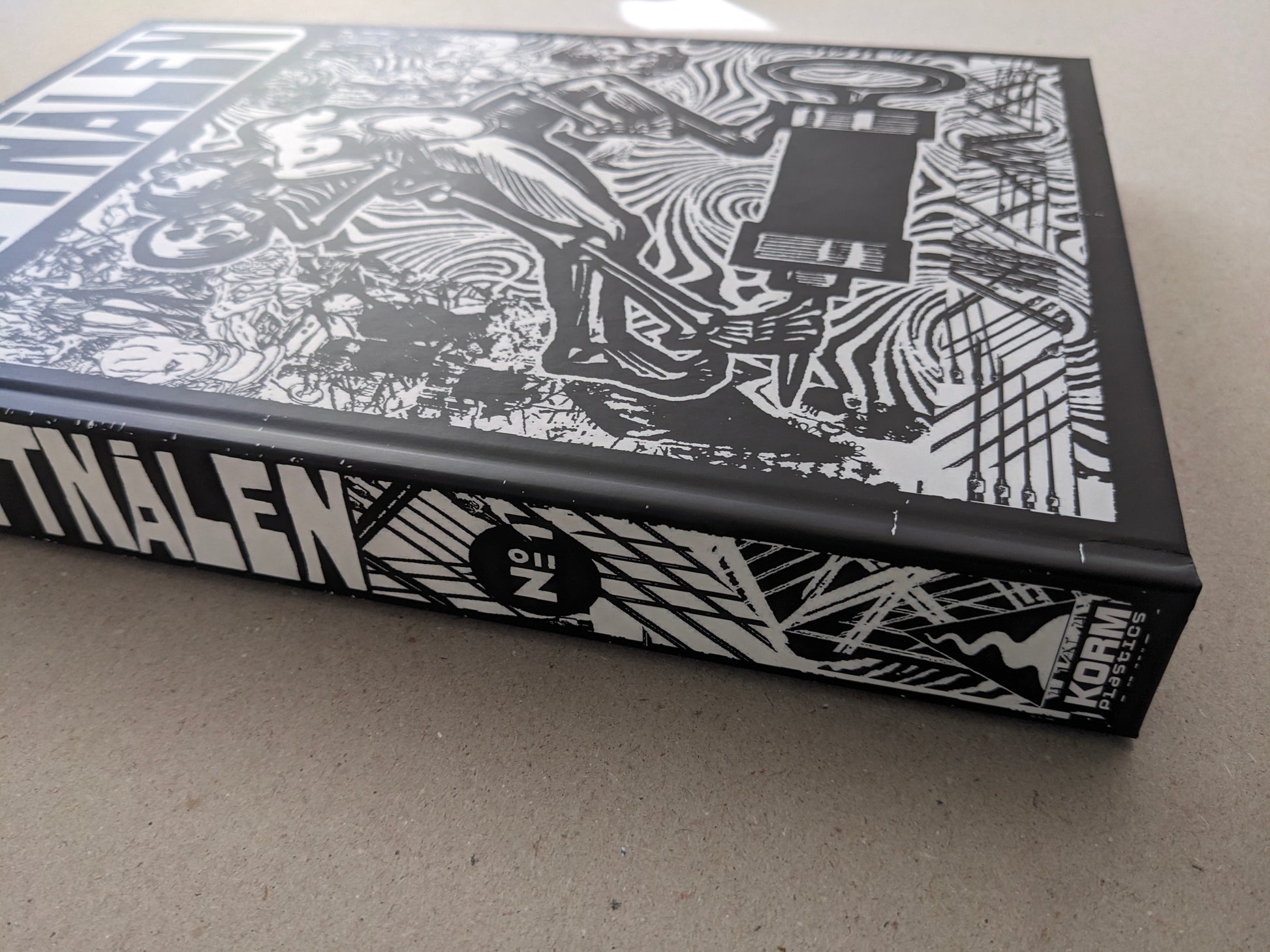 Spine view of the “GIFTNÅLEN” book by Kristian Olsson, black-and-white cover art visible along the edge.