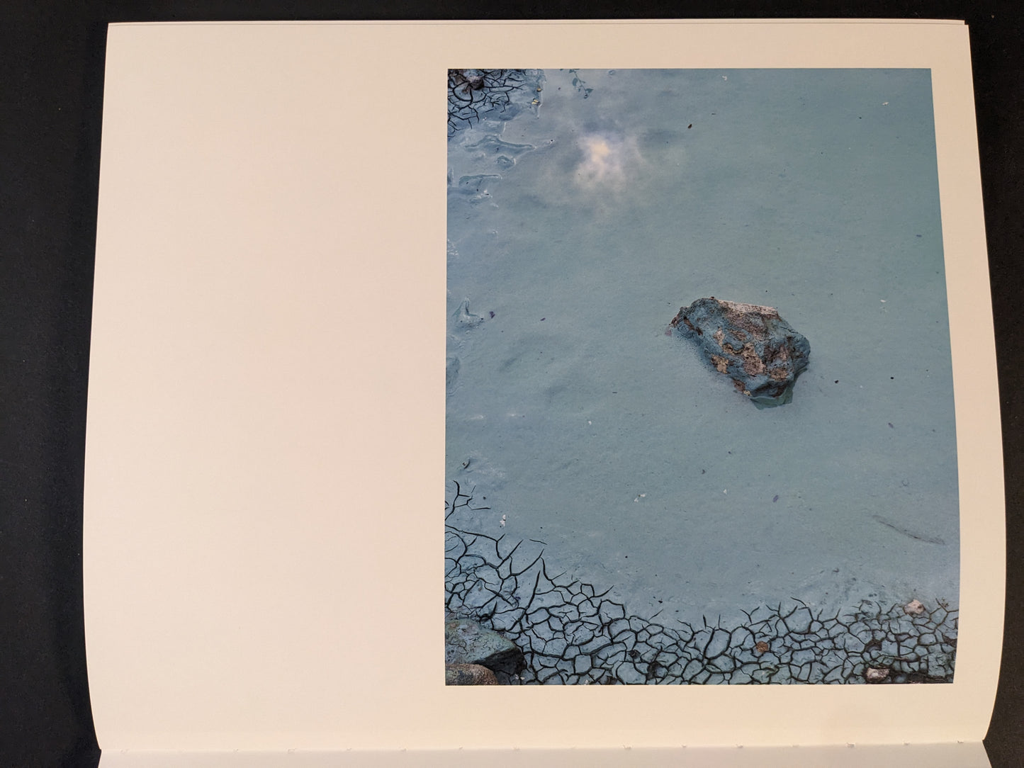 Interior page from Glass Mountain by Michael Lundgren, showing a rock in pale blue water with cracked mud at the edges