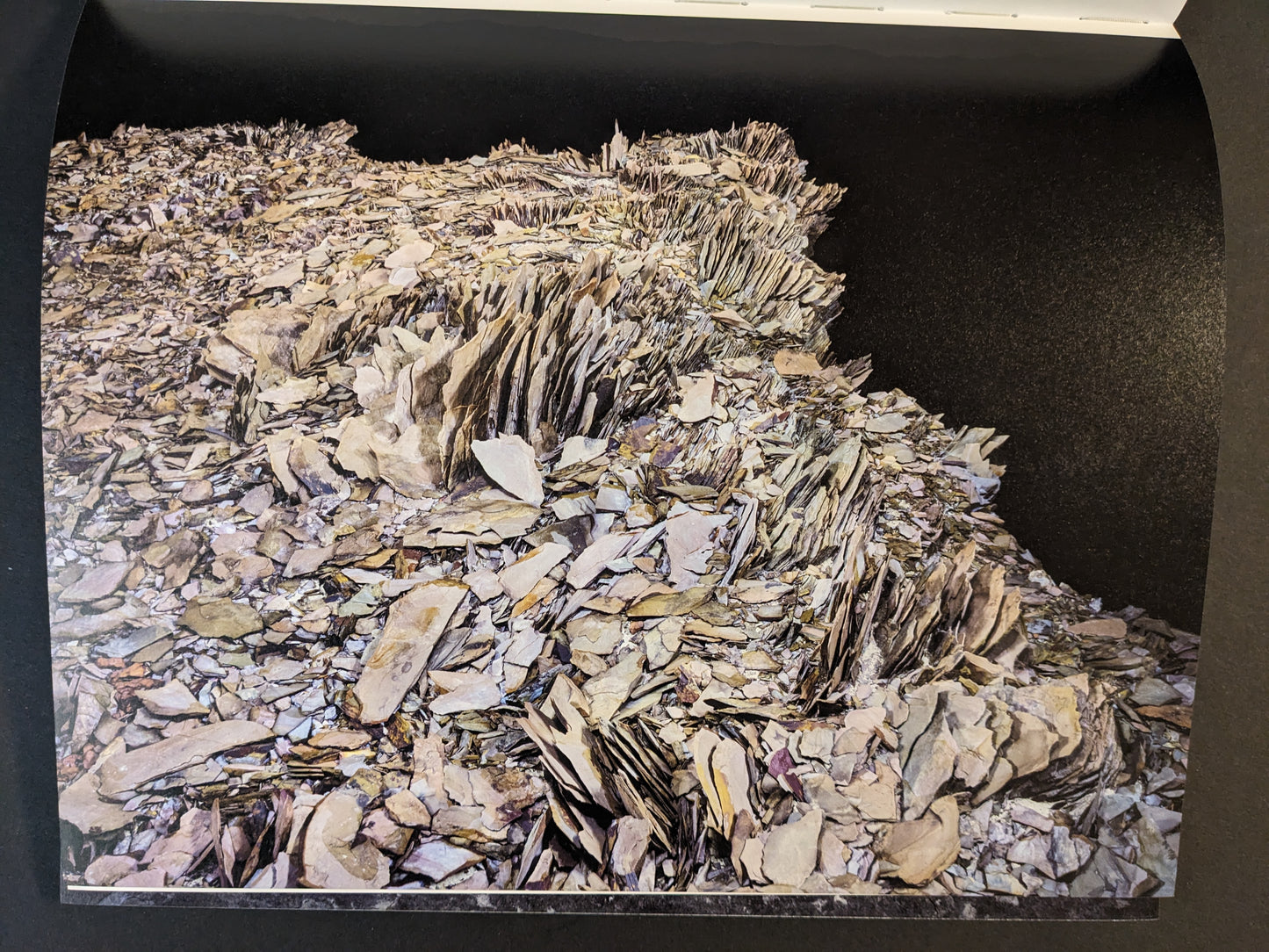 Interior photograph from Glass Mountain by Michael Lundgren, showing layered rock plates and fragments against a dark background