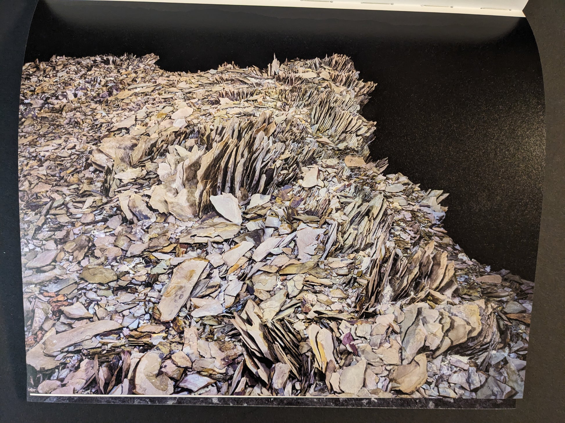 Interior photograph from Glass Mountain by Michael Lundgren, showing layered rock plates and fragments against a dark background