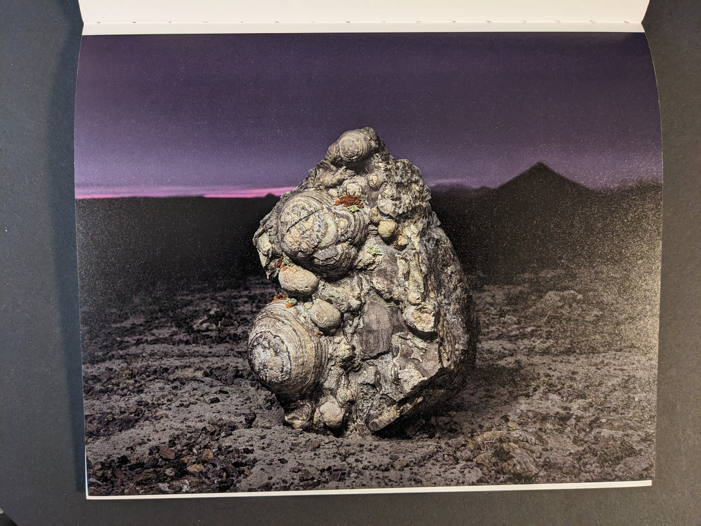 Interior photograph from Glass Mountain by Michael Lundgren, showing a textured rock on dark ground under a purple dusk sky