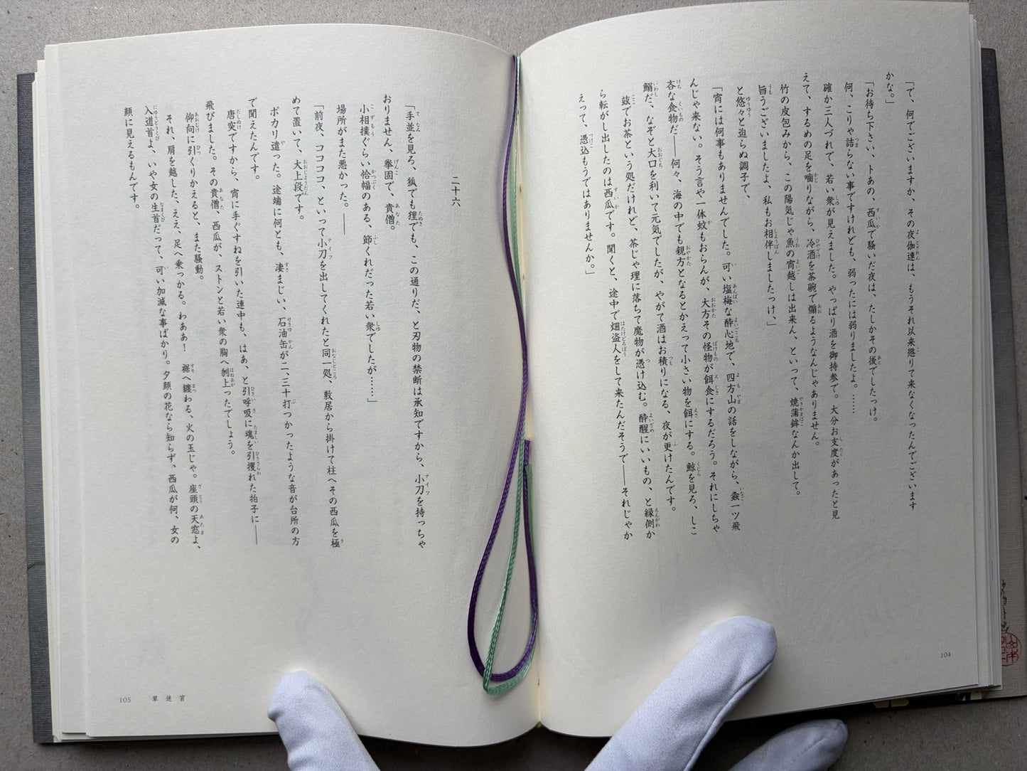 An open book Grass Labyrinth by Takato Yamamoto with Japanese text spread across both pages, held from below by gloved hands. A purple and green ribbon bookmark loops through the center of the pages.