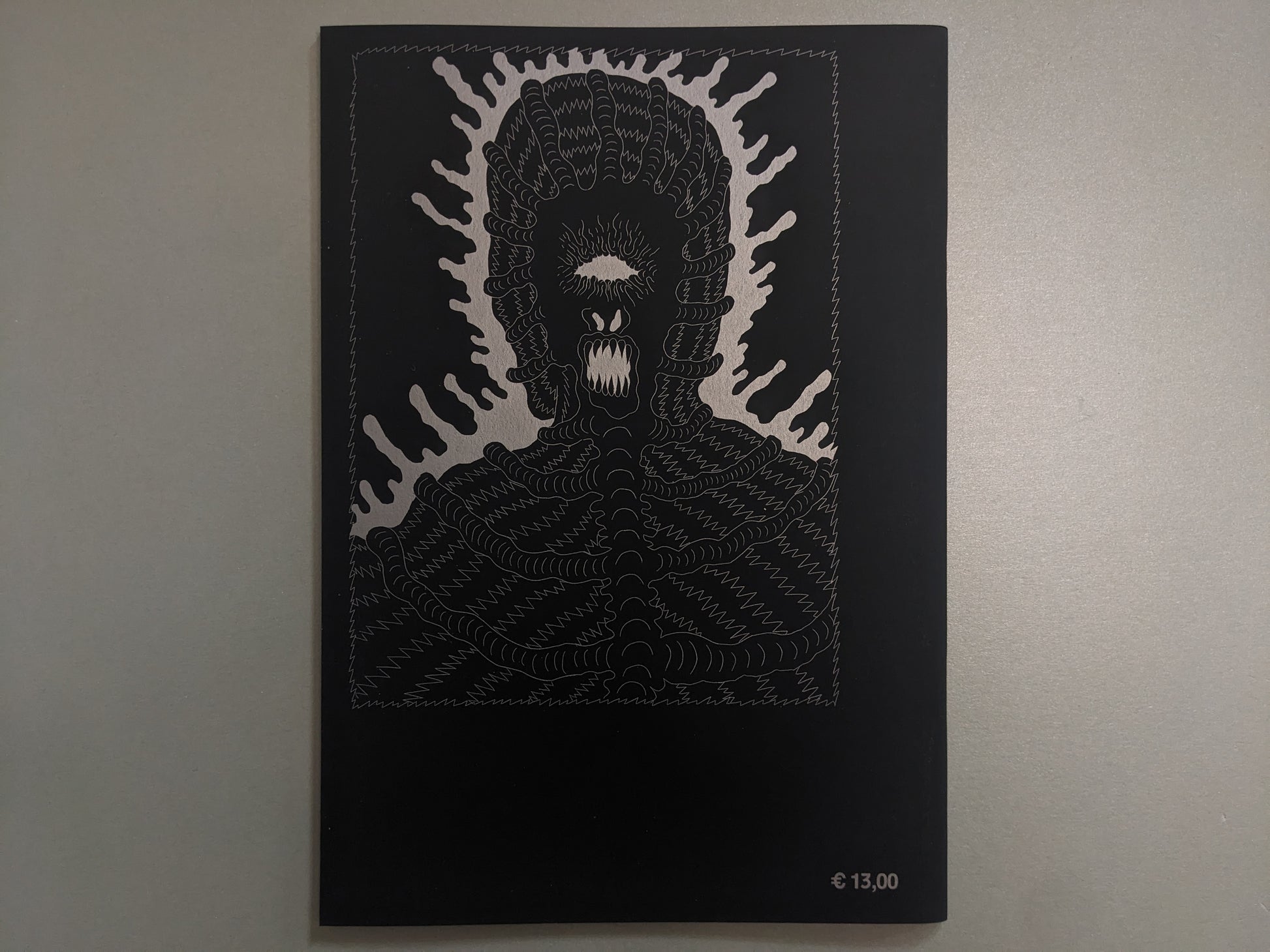 Back cover of Grayworld with a silver monster face and price mark on black paper