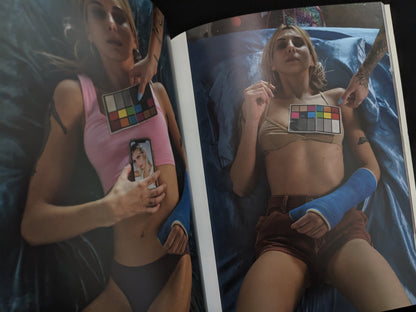 Two women lying on a bed, each with a color chart on their chest, from Richard Kern's photobook "Grey Cards".