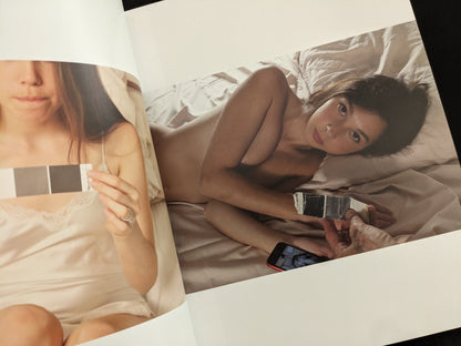 Nude portrait of a woman lying on a bed holding a grey card, from Grey Cards by Richard Kern