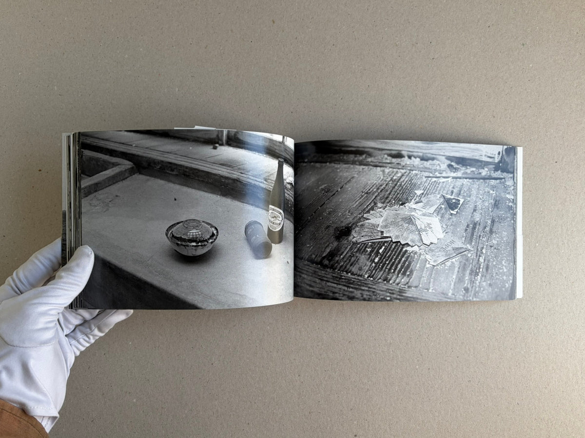 Open spread from Hashima - Taiji Matsue, showing two black-and-white photographs of objects on worn surfaces, held open by a gloved hand.