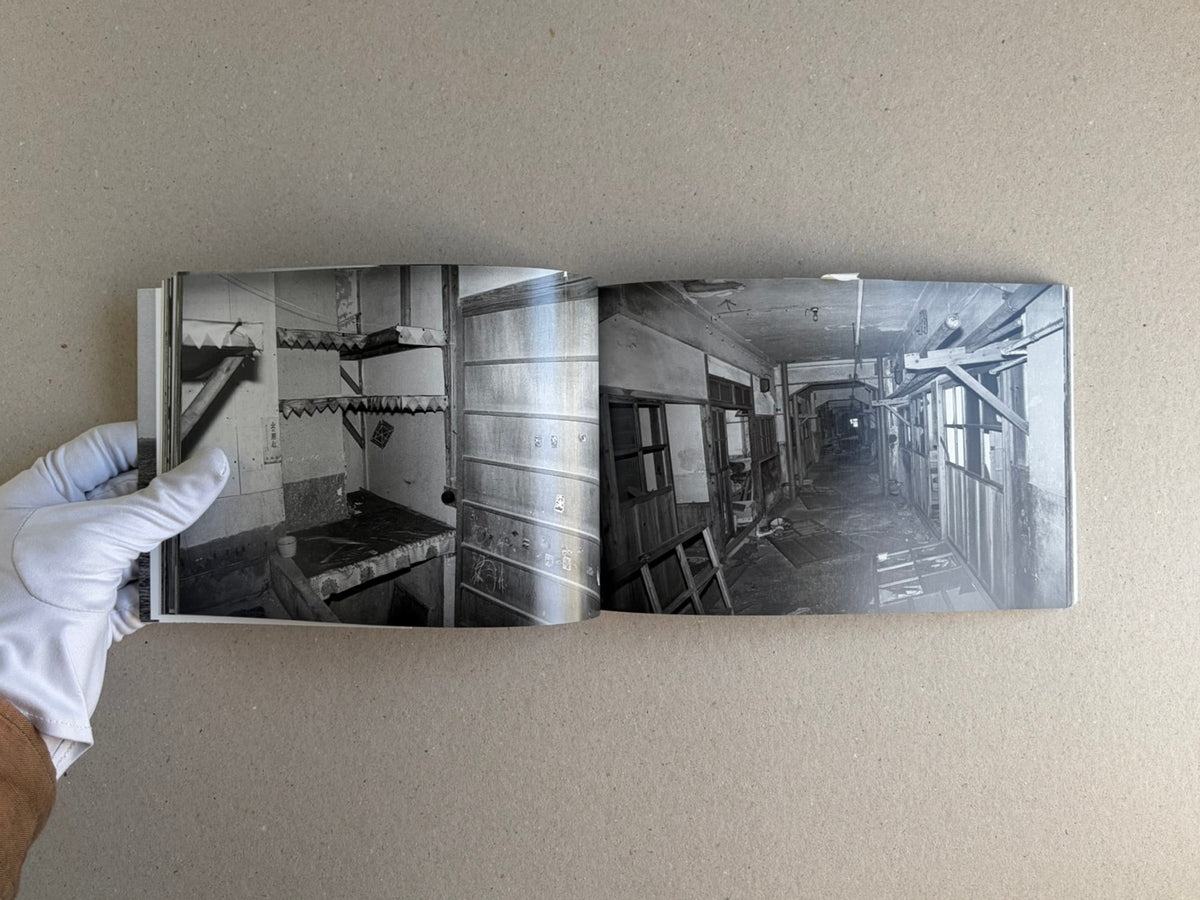 Open spread of Hashima - Taiji Matsue showing two black-and-white interior photographs in the book, held flat by a gloved hand.