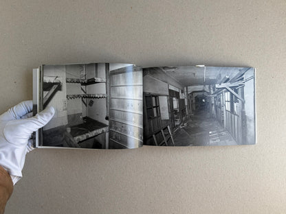 Open spread of Hashima - Taiji Matsue showing two black-and-white interior photographs in the book, held flat by a gloved hand.