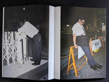 Two men sleeping standing and leaning over street barriers at night