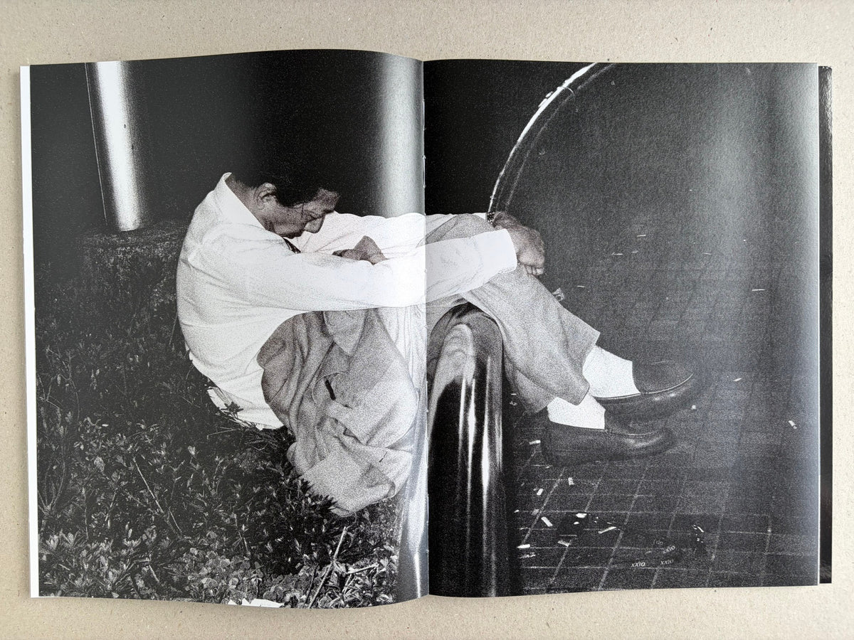 Black-and-white interior spread with a suited man curled up on the ground beside a post.