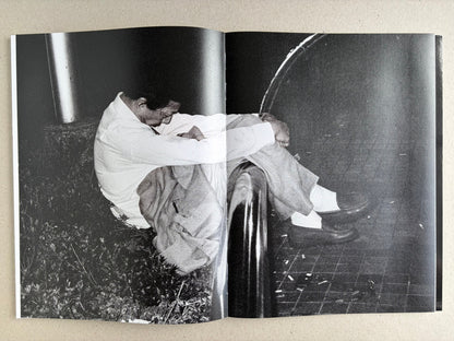 Black-and-white interior spread with a suited man curled up on the ground beside a post.