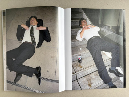 Interior spread with two colour photographs of sleeping suited men on pavement, one beside a drink bottle.