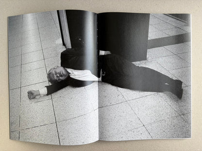 Black-and-white interior spread with a suited man lying on the floor beside a column.