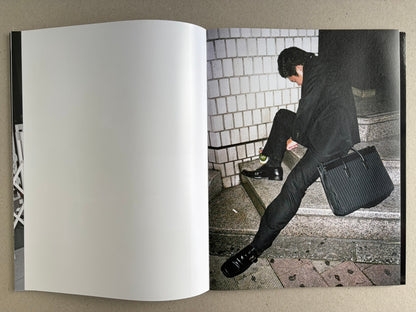 Interior spread with a blank left page and a colour photograph of a suited man sitting on steps beside a bag.
