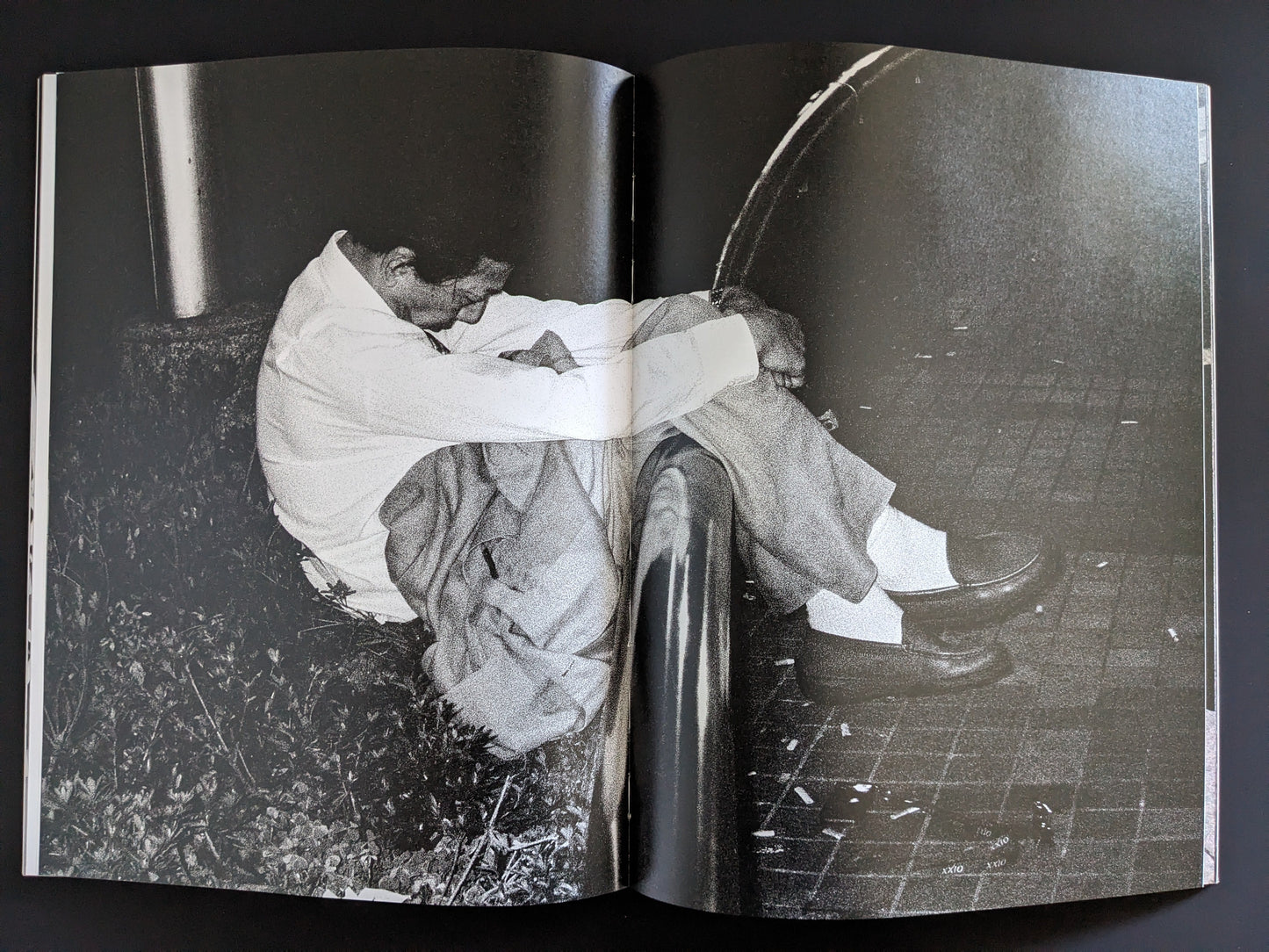 Open spread with a man in a white shirt sleeping in a crouched position on a metal rail at night