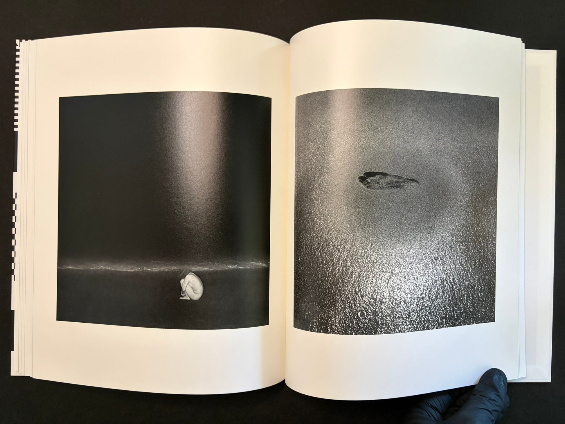 Open spread with a small figure at the bottom of a dark page and a small object on a textured grey page