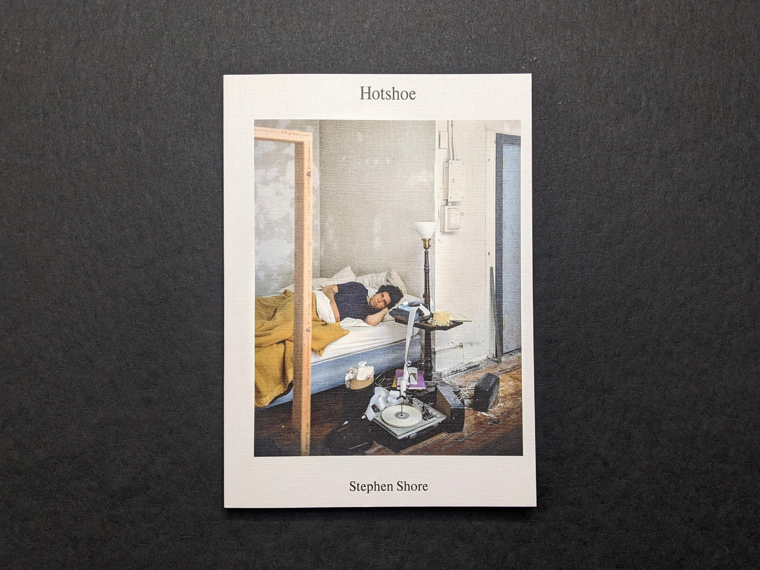 Front cover of Hotshoe Issue 214: Stephen Shore, showing a Stephen Shore colour photograph of a man lying on a bed in a sparse room.