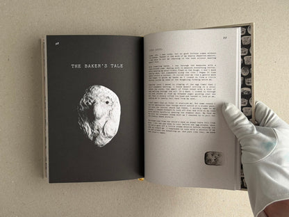 Open spread of How to Bake a Breadling by Brad Hock, showing page 98 with the title The Baker’s Tale and a sculptural bread-like form, and page 99 with text and a small image detail; a gloved hand holds the book open.