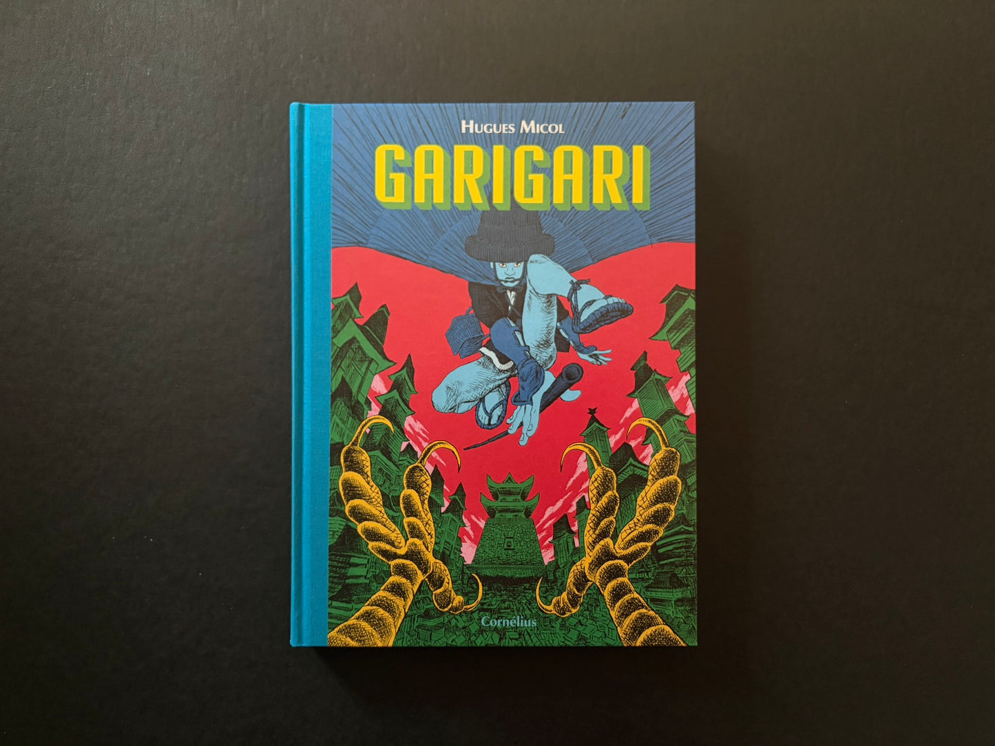 Hugues Micol – GariGari hardcover front cover on a black background, with a blue spine and a bright red and green samurai scene.
