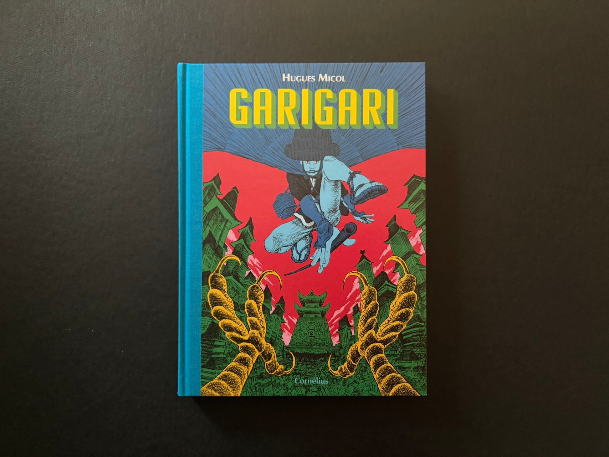 Hugues Micol – GariGari hardcover front cover on a black background, with a blue spine and a bright red and green samurai scene.