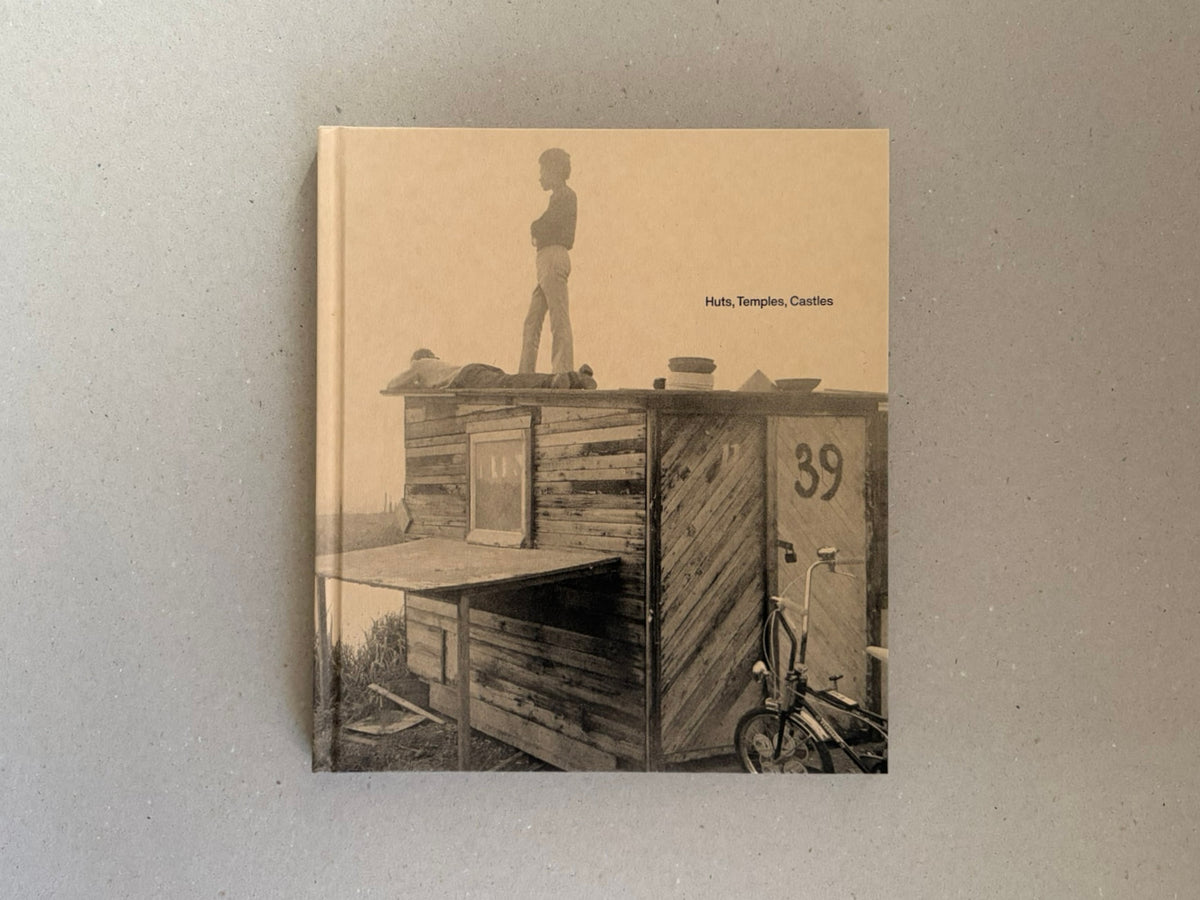 Cover of Huts, Temples, Castles by Ursula Schulz-Dornburg, showing a sepia-toned photograph of a wooden hut with a standing figure on the roof and the title printed on the front.