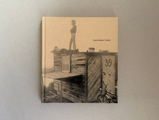 Cover of Huts, Temples, Castles by Ursula Schulz-Dornburg, showing a sepia-toned photograph of a wooden hut with a standing figure on the roof and the title printed on the front.