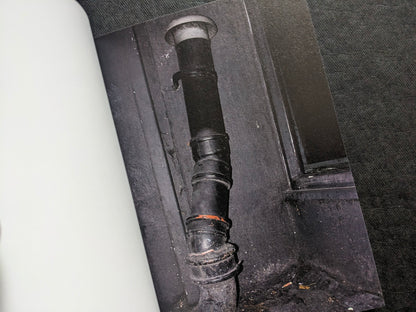 Close-up photograph of a dark drainpipe and wall detail.