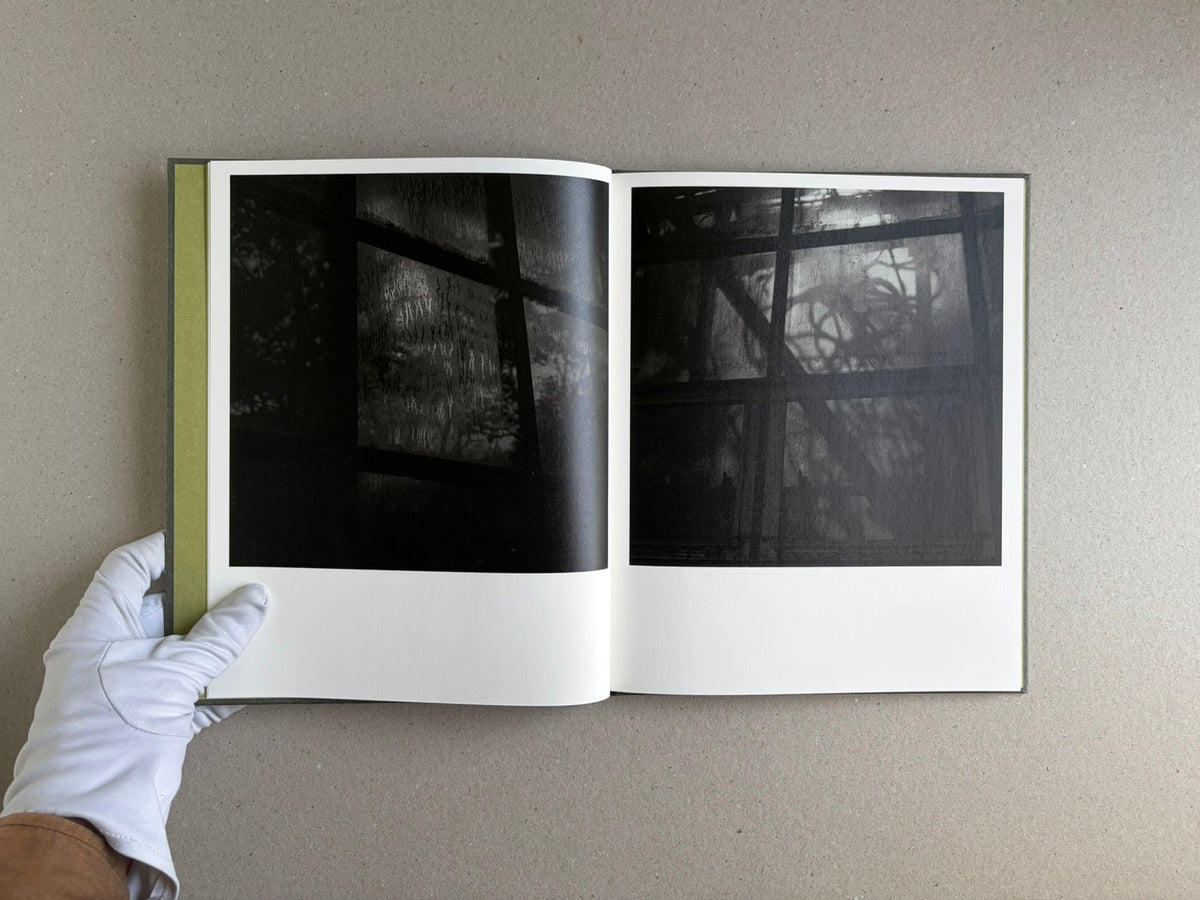 Open spread of Im Treibhaus by Takeshi Shinoda, showing two dark black-and-white photographs of greenhouse windows and plant shadows.