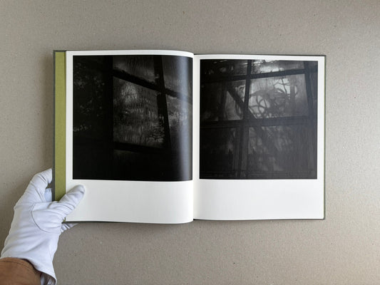 Open spread of Im Treibhaus by Takeshi Shinoda, showing two dark black-and-white photographs of greenhouse windows and plant shadows.