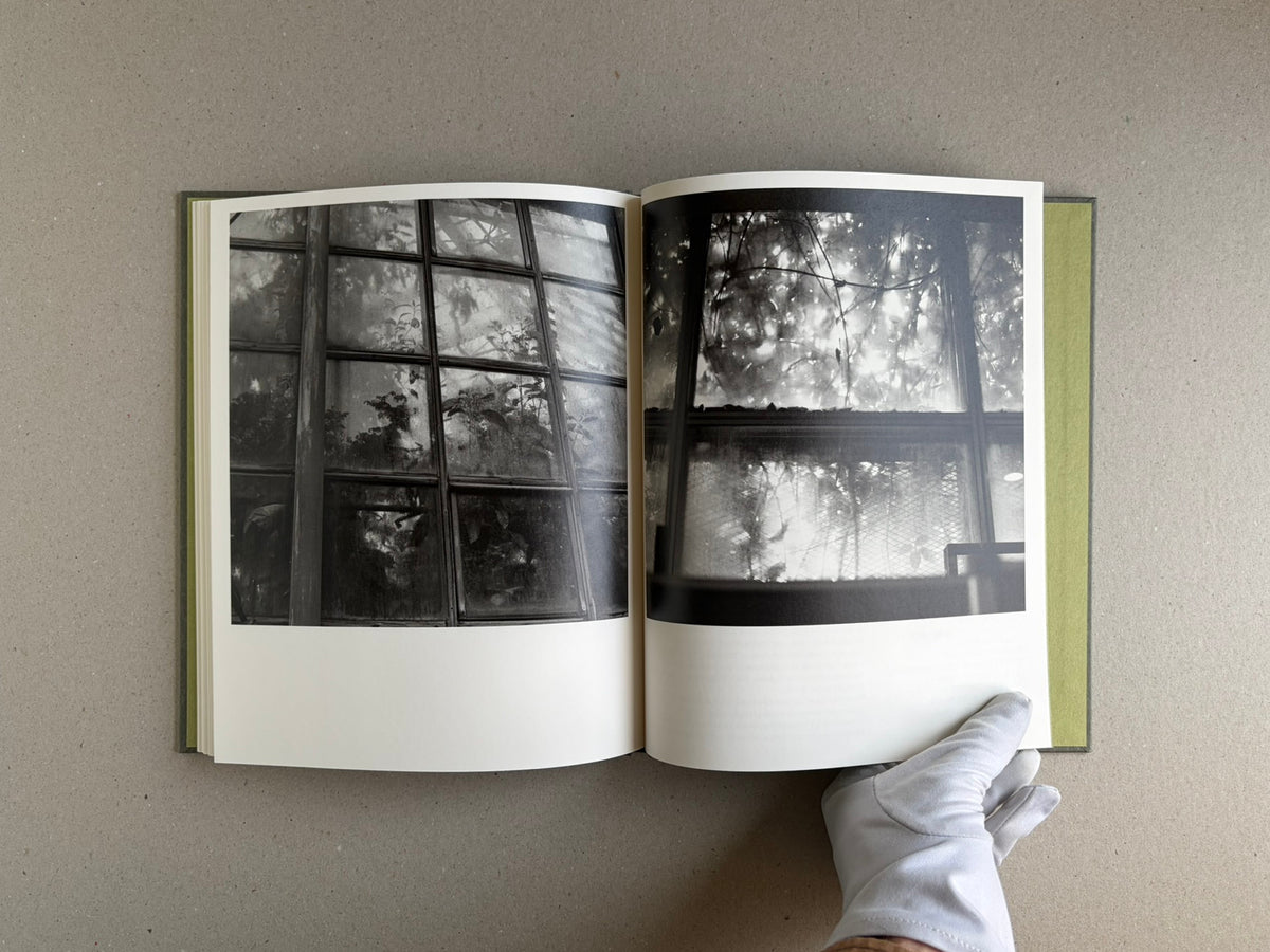 Open spread from Im Treibhaus by Takeshi Shinoda, showing two black-and-white greenhouse photographs with a gloved hand holding the lower right page.