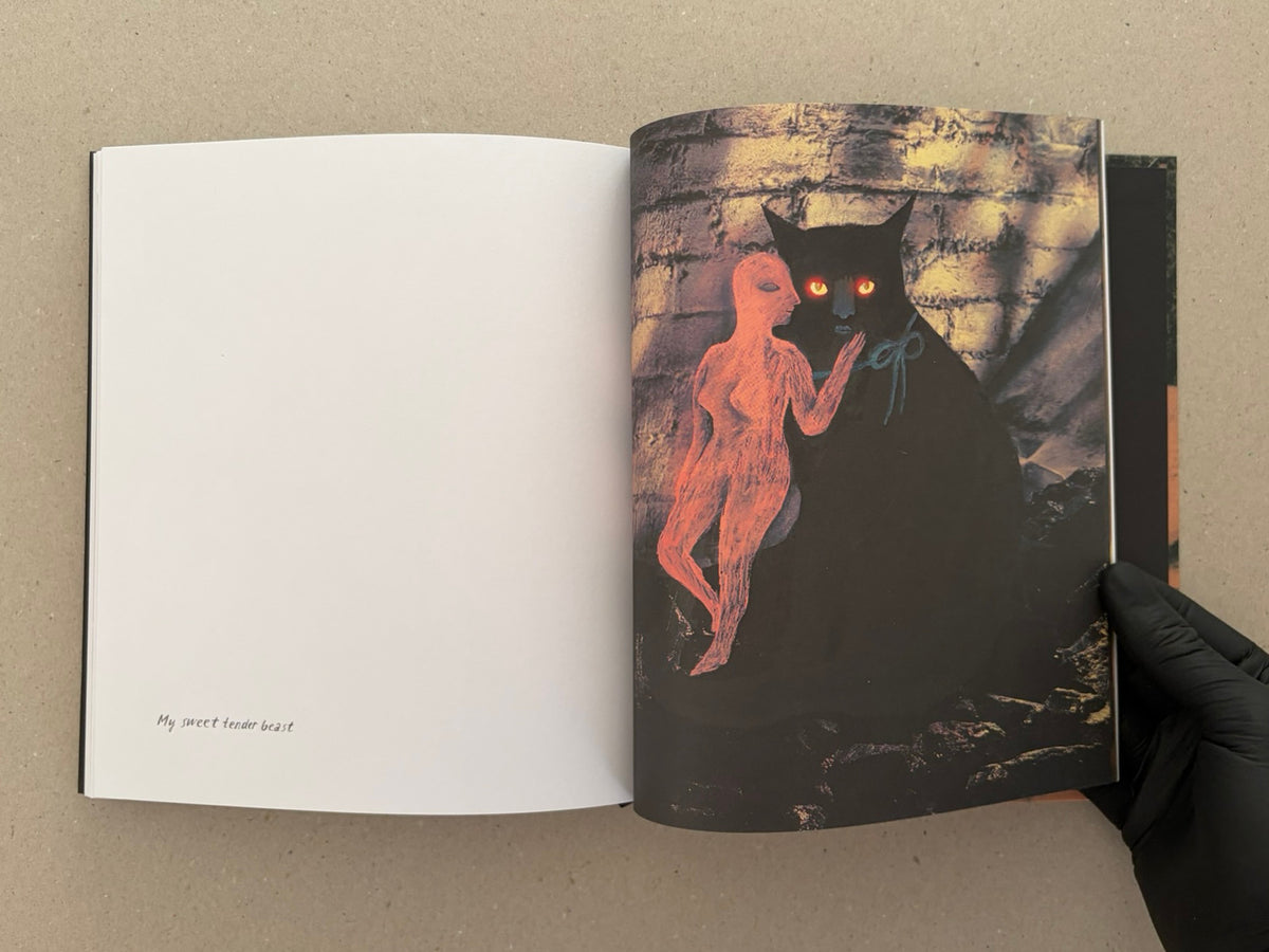 Open artbook spread from In a Dark Time, the Eye Begins to See – The Art of Julia Soboleva, with a blank left page and a right-page collage of a black cat with glowing eyes and a pink figure against a brick wall.