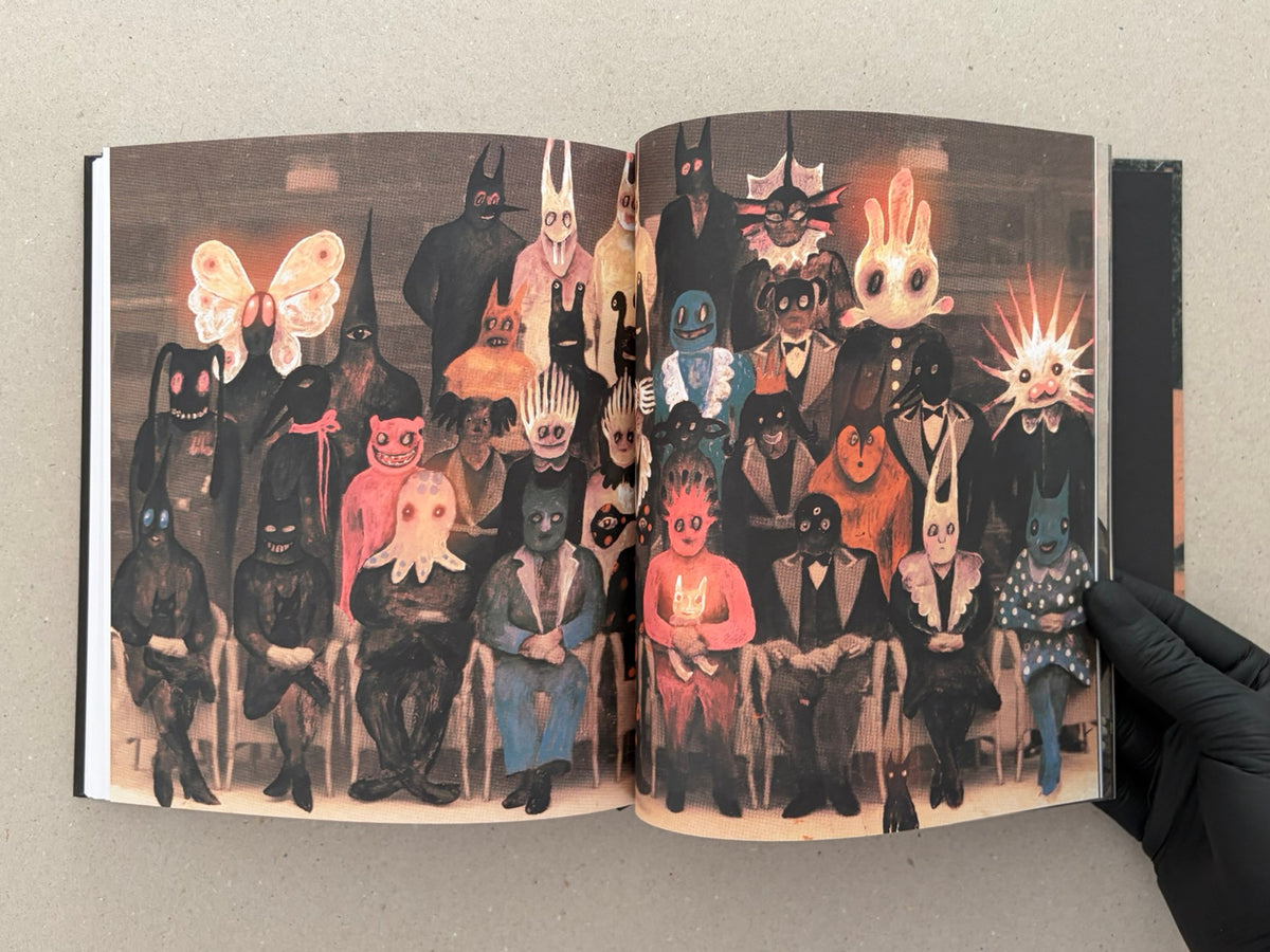 Open book spread from In a Dark Time, the Eye Begins to See – The Art of Julia Soboleva, showing a full-bleed image of a group of masked and animal-headed figures seated in rows.