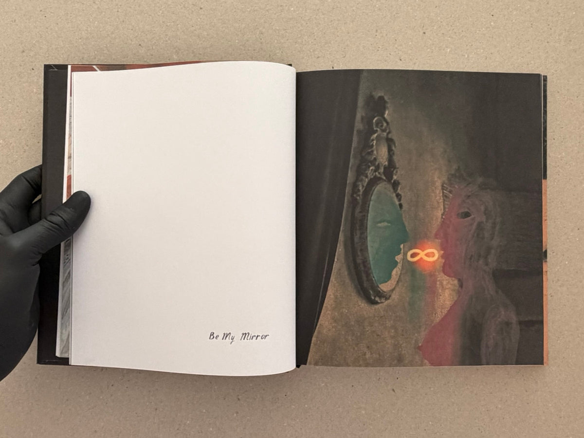 Open spread from In a Dark Time, the Eye Begins to See – The Art of Julia Soboleva, showing a blank left page with the caption “Be My Mirror” and a right page with a dark mixed-media image.