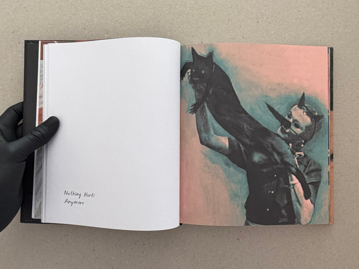 Open spread from In a Dark Time, the Eye Begins to See – The Art of Julia Soboleva, showing a blank left page with the text “Nothing Hurts Anymore” and a right-page mixed-media image in dark tones.